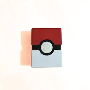 May include: A rectangular storage box featuring a red top half and a white bottom half, separated by a horizontal black band. In the centre of the black band is a circular white button with a thin black outline, mimicking a classic ball design.