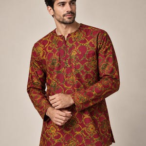 May include: A long-sleeved shirt featuring a deep red base color with a repeating circular and floral pattern in shades of mustard yellow and olive green. The shirt has a round neckline with a small vertical slit and a single chest pocket.