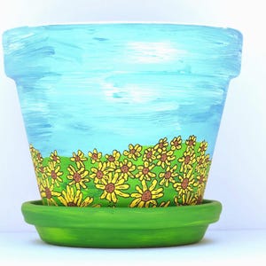 May include: A white ceramic mug with a black handle and the text "But First, Coffee" in a bold, black font. The mug is set against a blurred background, suggesting a cozy setting. The mug appears to be approximately 4 inches tall.