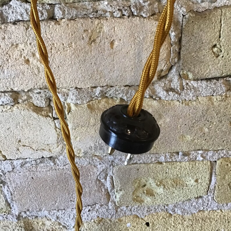 May include: Close-up of a black electrical plug with a gold braided cord. The plug is attached to a wall.