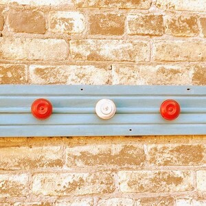 May include: A light blue wooden shelf with five white and red ceramic knobs. The shelf is mounted on a brick wall. A glass jar is attached to the left side of the shelf.