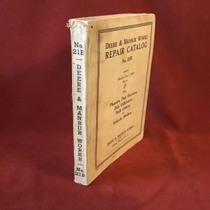 May include: A vintage book titled "Deere & Mansur Works Repair Catalog" with the number 21B on the cover. The book is for planters, disk harrows, disk cultivators, stalk cutters, and endgate seeders.