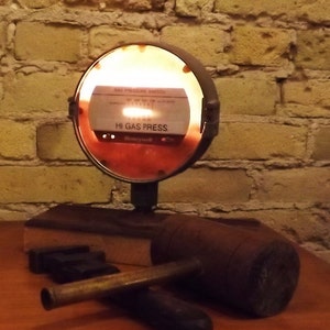 May include: A vintage gas pressure switch with a red and white face, illuminated from behind, mounted on a wooden base with a brown wooden mallet. The switch reads "Gas Pressure Switch" and "Hi Gas Press" with the Honeywell logo.