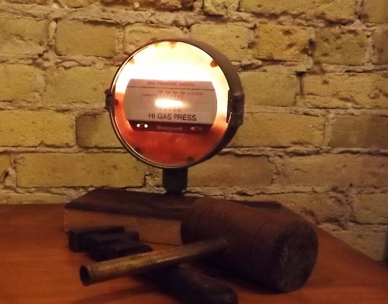 May include: A vintage gas pressure switch with a red and white face, illuminated from behind, mounted on a wooden base with a brown wooden mallet. The switch reads "Gas Pressure Switch" and "Hi Gas Press" with the Honeywell logo.