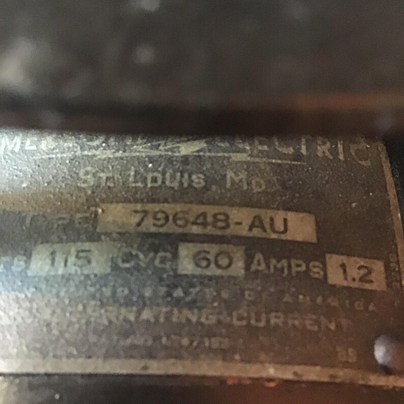 May include: Close-up of a metal plate with the text "St. Louis, Mo" and the number "79648-AU". The plate also includes the text "115 CYC 60 AMPS 1.2" and the words "ALTERNATING CURRENT".