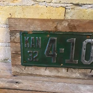 May include: A vintage green Kansas license plate with the number 4-10 and the year 32. The plate is mounted on a piece of weathered wood.