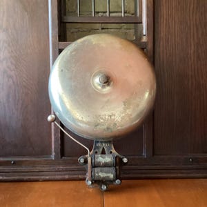 May include: A vintage circular metal bell with a polished brass finish and a central bolt. The mechanism features a small striker arm and two exposed electromagnetic coils at the base, with the text NO. 612 clearly embossed on the metal frame.