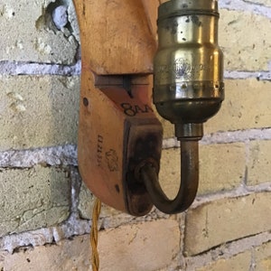 May include: A vintage wooden wall sconce with a brass light socket and a brown cord. The sconce has the text "E121 33" and "OAA" printed on it.