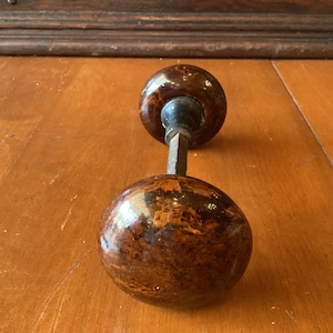 May include: Antique door knob with a brown and tan marbled pattern. The knob has a round shape and is attached to a metal rod. The door knob is a vintage item, likely made of ceramic or a similar material.