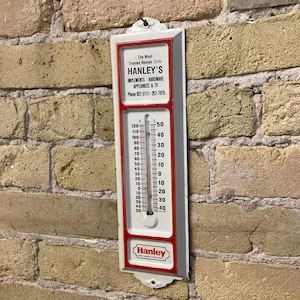 May include: A vintage white and red thermometer with the text "HANLEY'S" and temperature readings in Fahrenheit and Celsius. The thermometer is mounted on a brick wall. The temperature reads approximately 70 degrees Fahrenheit.