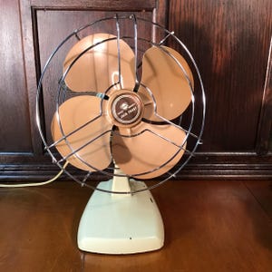 May include: Vintage Jack Frost electric fan with tan blades and a chrome cage. The fan has a mint green base and a brown center with the words "Jack Frost". A classic appliance for cooling.