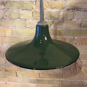 Puede incluir: Una lámpara colgante industrial vintage de color verde oscuro con una pantalla ancha y acampanada. La luz está suspendida de un tubo metálico.