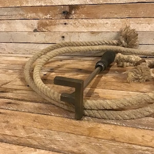 May include: A metal branding iron shaped like the letter "F" with a wooden handle, lying on a wooden surface with a coiled rope.
