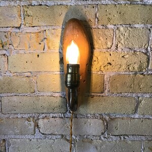 May include: A wooden shoe-shaped wall sconce with a light bulb and a cord. The shoe is brown and has the number 8 and the letters AA on it.