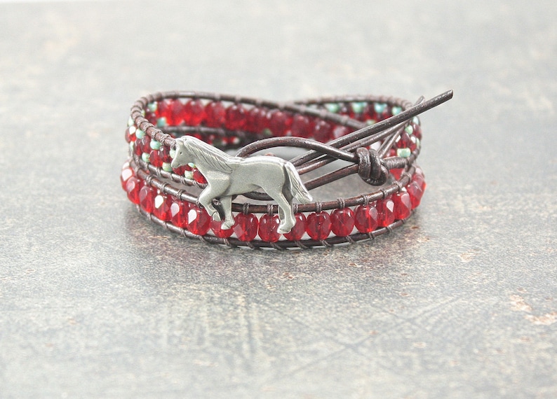 May include: A brown leather wrap bracelet with red and turquoise beads and a silver horse charm.