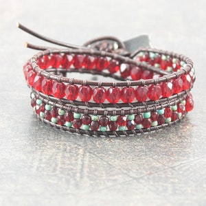 May include: A brown leather wrap bracelet with red and turquoise beads. The bracelet is made with multiple strands of leather and beads, creating a layered effect.