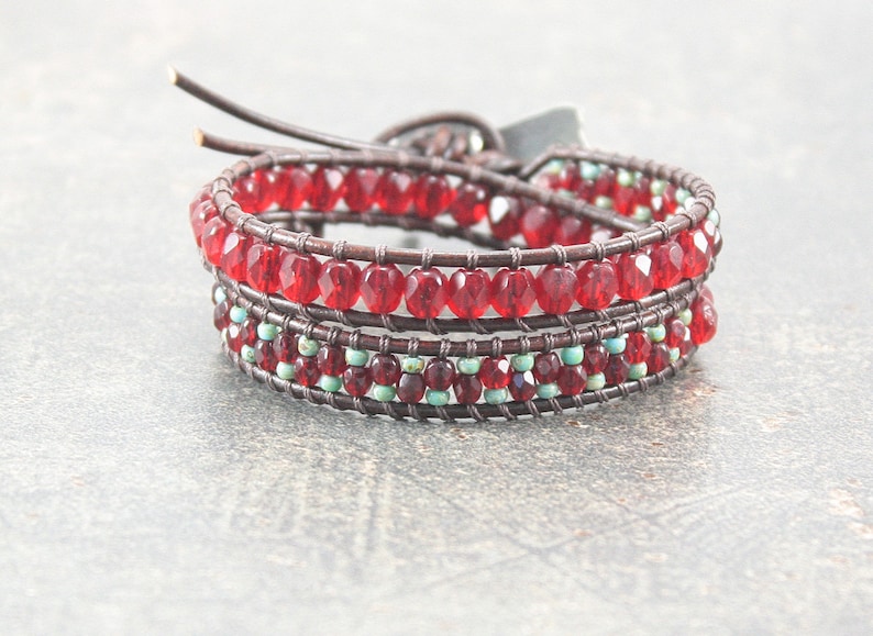 May include: A brown leather wrap bracelet with red and turquoise beads. The bracelet is made with multiple strands of leather and beads, creating a layered effect.