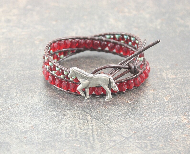 May include: A red and brown leather wrap bracelet with a silver horse charm. The bracelet is made with small red glass beads and has a leather tie closure.