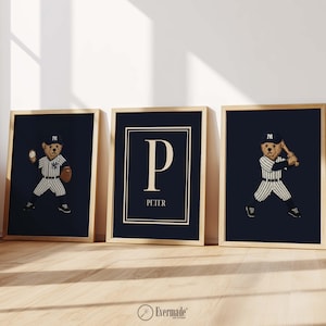 Puede incluir: Tres impresiones enmarcadas con marcos dorados. Dos impresiones presentan un oso de peluche con uniforme de béisbol. La tercera impresión tiene la letra "P" y el nombre "PETER". Todas las impresiones tienen un fondo azul marino.