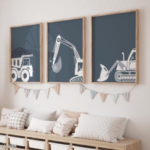 Puede incluir: Tres láminas enmarcadas con vehículos de construcción: un camión volquete, una excavadora y una cargadora frontal. Cada lámina tiene un fondo azul marino con ilustraciones blancas y grises. Los marcos son de color marrón claro.