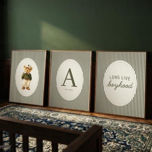 May include: Three framed wall art pieces with a green and white striped background. One features a teddy bear in a cap and outfit, another has the letter "A", and the third reads "LONG LIVE boyhood". The frames are brown.