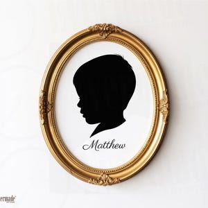 May include: A gold oval frame with a black silhouette of a child's profile. The child's name, Matthew, is written in cursive below the silhouette. The frame has ornate detailing and is set against a white background.
