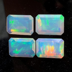 Może przedstawiać: Cztery prostokątne opale z iryzującą grą kolorów. Kamienie szlachetne są osadzone na ciemnym tle, prezentując ich żywe wewnętrzne kolory zieleni, pomarańczy i błękitu. Opale mają wypolerowaną, gładką powierzchnię.
