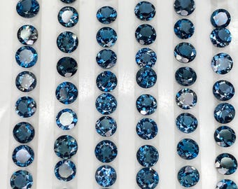 Pode incluir: Coleção de pedras preciosas azuis redondas e ovais dispostas em fileiras. As gemas variam em tons de azul claro a escuro, com facetas brilhantes. A disposição sugere uma exibição de pedras preciosas soltas.