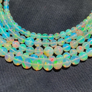 May include: Close-up of several strands of iridescent opal beads. The beads are round and vary in size, displaying a play of color with hues of blue, green, and red. The background is a dark, textured fabric.