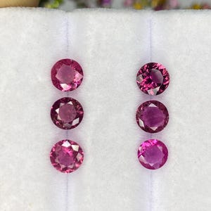 Puede incluir: Seis gemas redondas y facetadas en tonos rosa y magenta se muestran sobre una superficie blanca. Las gemas tienen un corte brillante, que refleja la luz. Adecuado para la fabricación de joyas o colecciones.