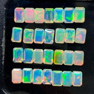 Könnte beinhalten: Eine Sammlung rechteckiger Opale mit schillernden Farben wie Grün, Blau und Rosa. Die Opale sind in Reihen angeordnet und zeigen ihre polierten Oberflächen und das innere Farbspiel. Die Edelsteine sind vor einem dunklen Hintergrund platziert.