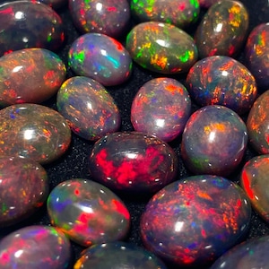 May include: A collection of polished black opals with vibrant flashes of color. The opals display a range of hues, including red, green, blue, and orange, creating a dazzling display. The gemstones are oval-shaped and have a glossy surface.
