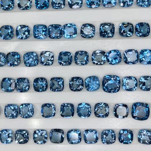 Puede incluir: Filas de gemas azul claro, de corte cuadrado, se exhiben en una bandeja blanca. Las gemas tienen un ligero brillo y están dispuestas en filas ordenadas, mostrando su forma y color uniformes. Las gemas son probablemente para la fabricación de joyas.