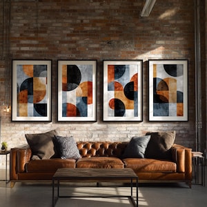 May include: Four framed abstract art prints with geometric shapes in orange, blue, black, and tan hues hang above a brown leather tufted sofa. A wooden coffee table and side table are in front of the sofa, set against a brick wall.
