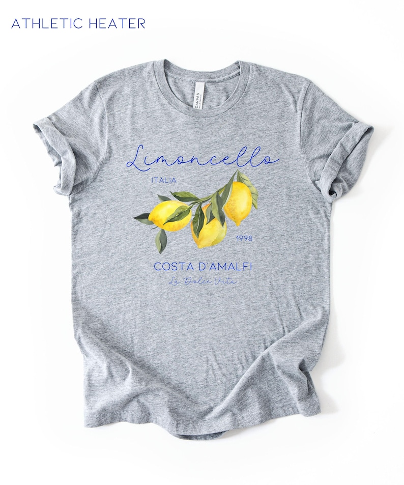 Puede incluir: Camiseta gris con la frase "Limoncello Italia 1998 Costa D'Amalfi" en azul. La camiseta presenta una ilustraci&oacute;n de acuarela de limones en una rama. El texto "Athletic Heather" est&aacute; en la parte superior.
