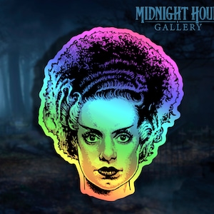 May include: A rainbow holographic sticker featuring a black and white illustration of the Bride of Frankenstein. The sticker has a black outline and a rainbow gradient background.