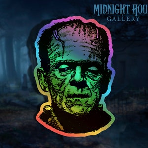 May include: A holographic sticker featuring a green and black illustration of Frankenstein's monster. The sticker has a rainbow border and the text "MIDNIGHT HOUR GALLERY" at the top.