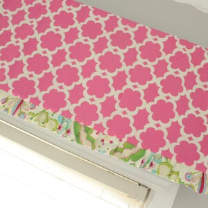 May include: A pink and white patterned valance with a ruffled edge. The valance is trimmed with a floral fabric in shades of green, blue, and pink.
