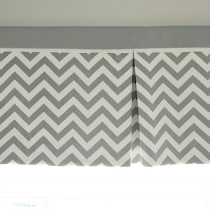 May include: A gray and white chevron patterned valance. The valance is mounted above a window and has a solid gray top section. The chevron pattern is a repeating zigzag design.
