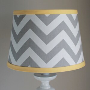 May include: A gray and white chevron patterned lampshade with a yellow trim.