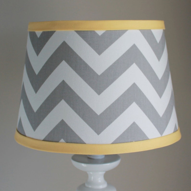 May include: A gray and white chevron patterned lampshade with a yellow trim.