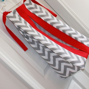 May include: A gray and white chevron patterned diaper bag with red ribbon ties.
