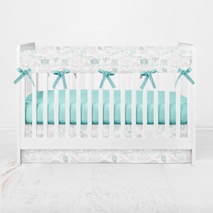 May include: A white crib with a turquoise and white floral crib bedding set. The bedding includes a bumper, fitted sheet, and skirt.