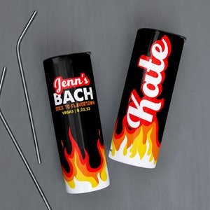 May include: Two black and white insulated tumblers with flames and text. One tumbler says "Jenn's Bach Goes to Flavortown Vegas 8.22.23". The other tumbler says "Hottie".