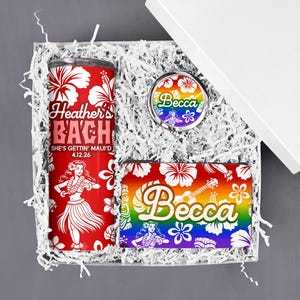 May include: A gift box with a red tumbler, a compact mirror, and a wallet, all with a Hawaiian theme. The tumbler reads "Heather's BACH" with a hula dancer and hibiscus flowers. The mirror and wallet feature the name "Becca" in a rainbow design.
