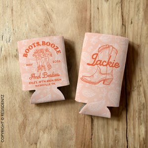 May include: Two pink and white can coolers with a paisley pattern. One cooler has the text "Boots, Booze" and "And Besties" with a drawing of three women in cowboy boots. The other cooler has the text "Jackie" with a drawing of a cowboy boot.
