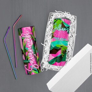 Pu&ograve; includere: Un bicchiere con motivo a foglie tropicali rosa e verde con il nome "Savannah" in lettere rosa neon. Il bicchiere &egrave; in una scatola regalo bianca con carta da imballaggio bianca. Due cannucce di metallo iridescenti sono accanto alla scatola.