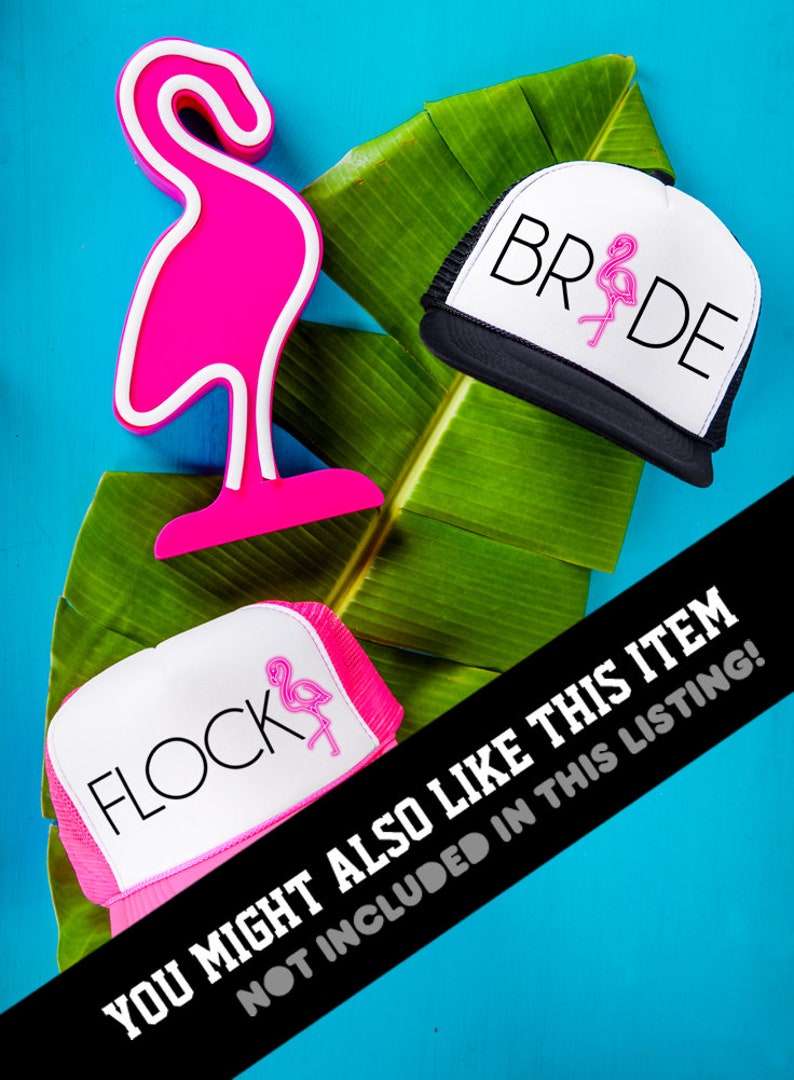 May include: Two pink and white trucker hats with flamingo designs. One hat says "Flock" and the other says "Bride". The hats are on a green leaf with a pink flamingo figurine.