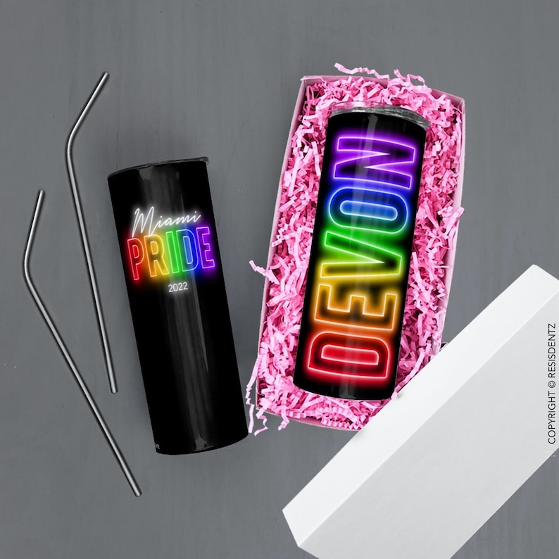K&ouml;nnte beinhalten: Zwei Edelstahlbecher mit Regenbogen-Designs. Ein Becher hat den Text "Miami Pride 2022" und der andere den Namen "Devon" in Regenbogenbuchstaben. Die Becher befinden sich in einer wei&szlig;en Box mit rosa Seidenpapier.