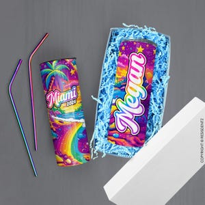 May include: Two stainless steel straws and two insulated tumblers. One tumbler features a colorful Miami 2026 design with a palm tree, rainbow, and stars. The other tumbler, in a gift box, has the name "Megan" in a vibrant design.
